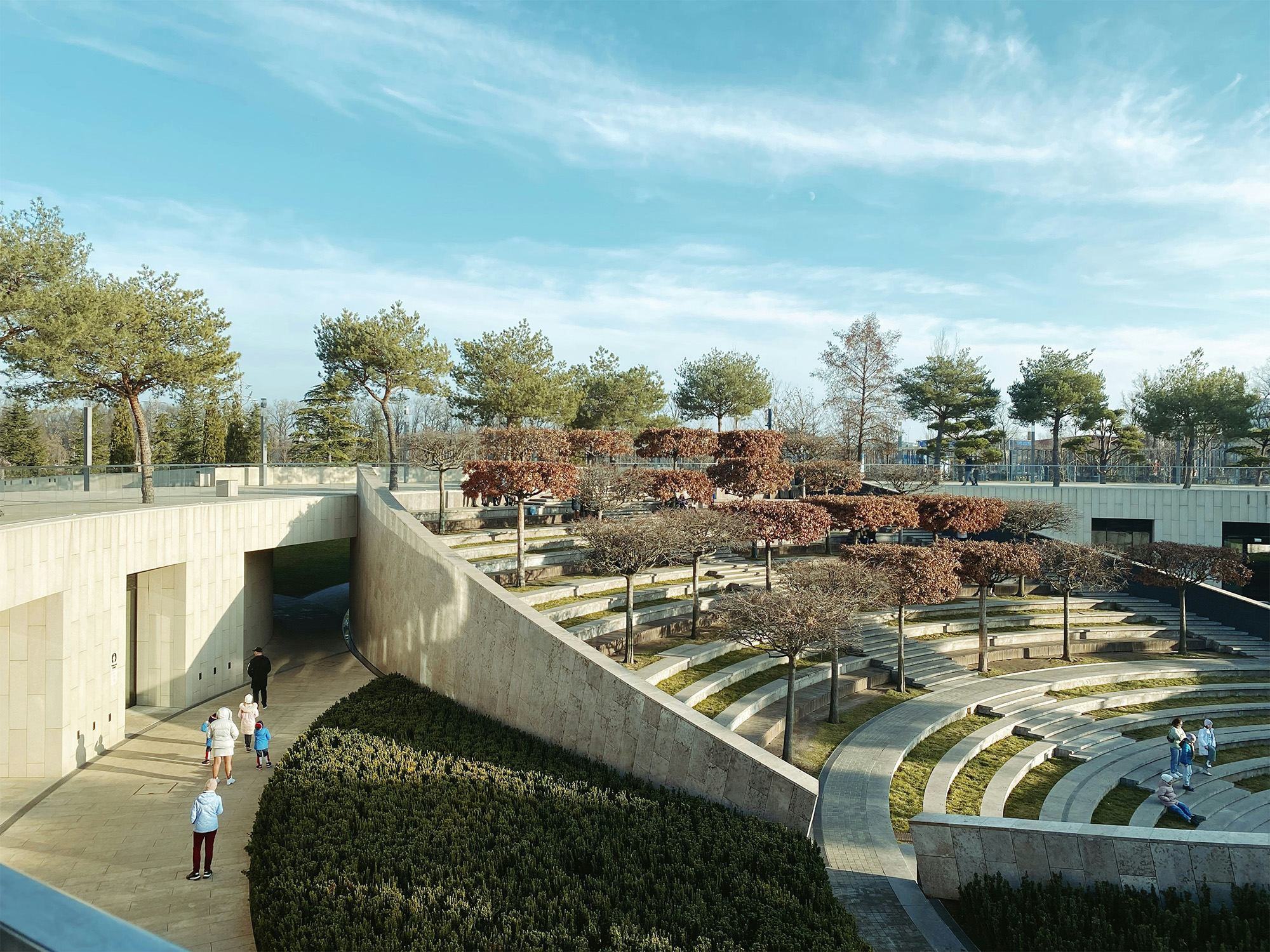 Modern park landscape with curved pathways, trees, and visitors enjoying the serene environment.