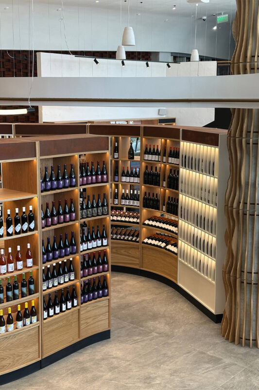 Curved wooden shelves display a variety of wine bottles in a modern retail space.