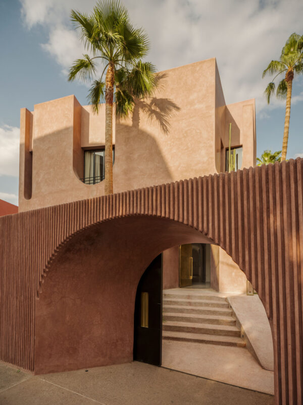 Modern architectural building with textured pink walls, palm trees, and a curved entrance leading to stairs.