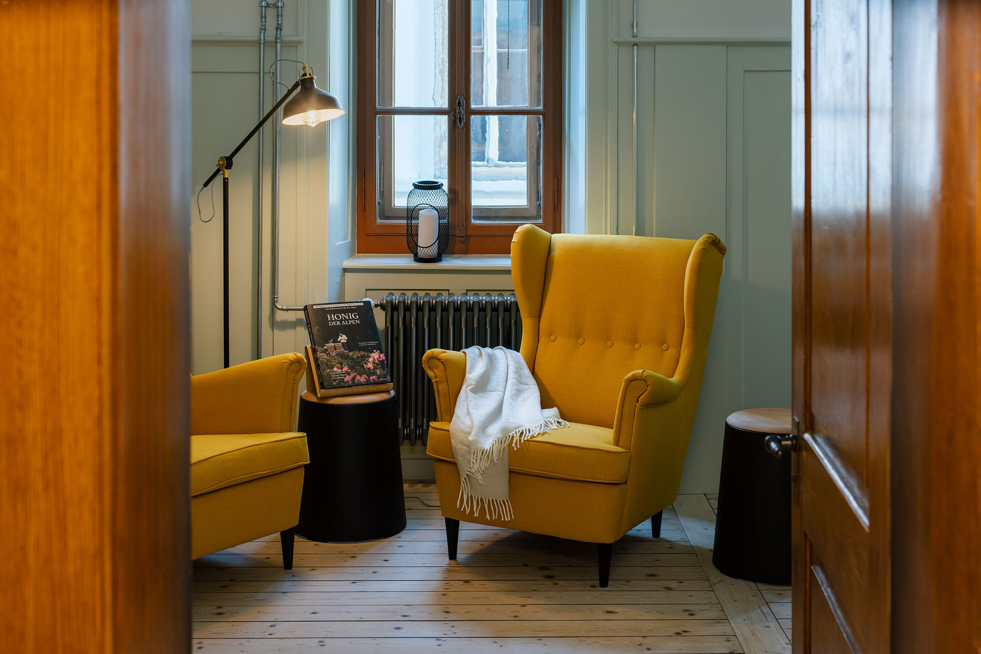 Cozy reading nook with two yellow armchairs, a small black table, a lamp, and a book on a wooden floor.