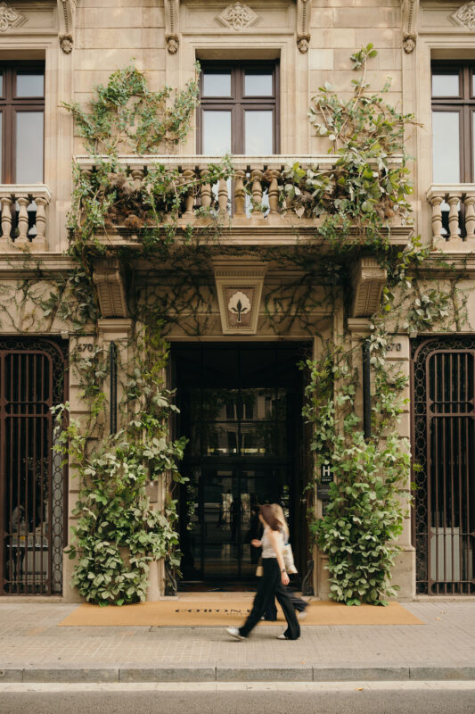 Facade of the Cotton House Hotel, adorned with greenery and a person walking by.