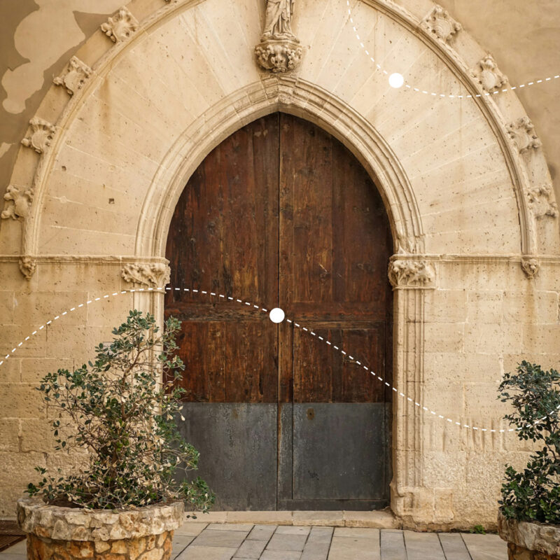 Wooden double doors set in a stone archway, flanked by potted plants, with decorative lines and dots overlaying the image.