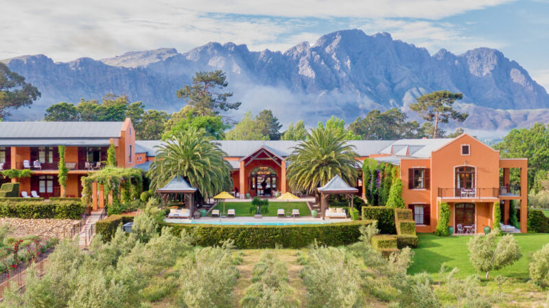 Aerial view of La Residence, featuring orange buildings, palm trees, and a pool, set against a mountainous backdrop.