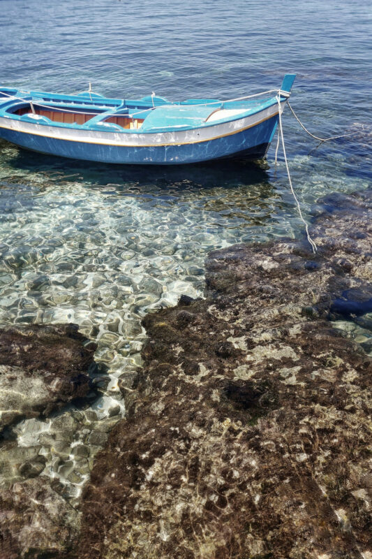 A blue boat anchored near rocky shorelines in clear water, showcasing the vibrant underwater landscape.