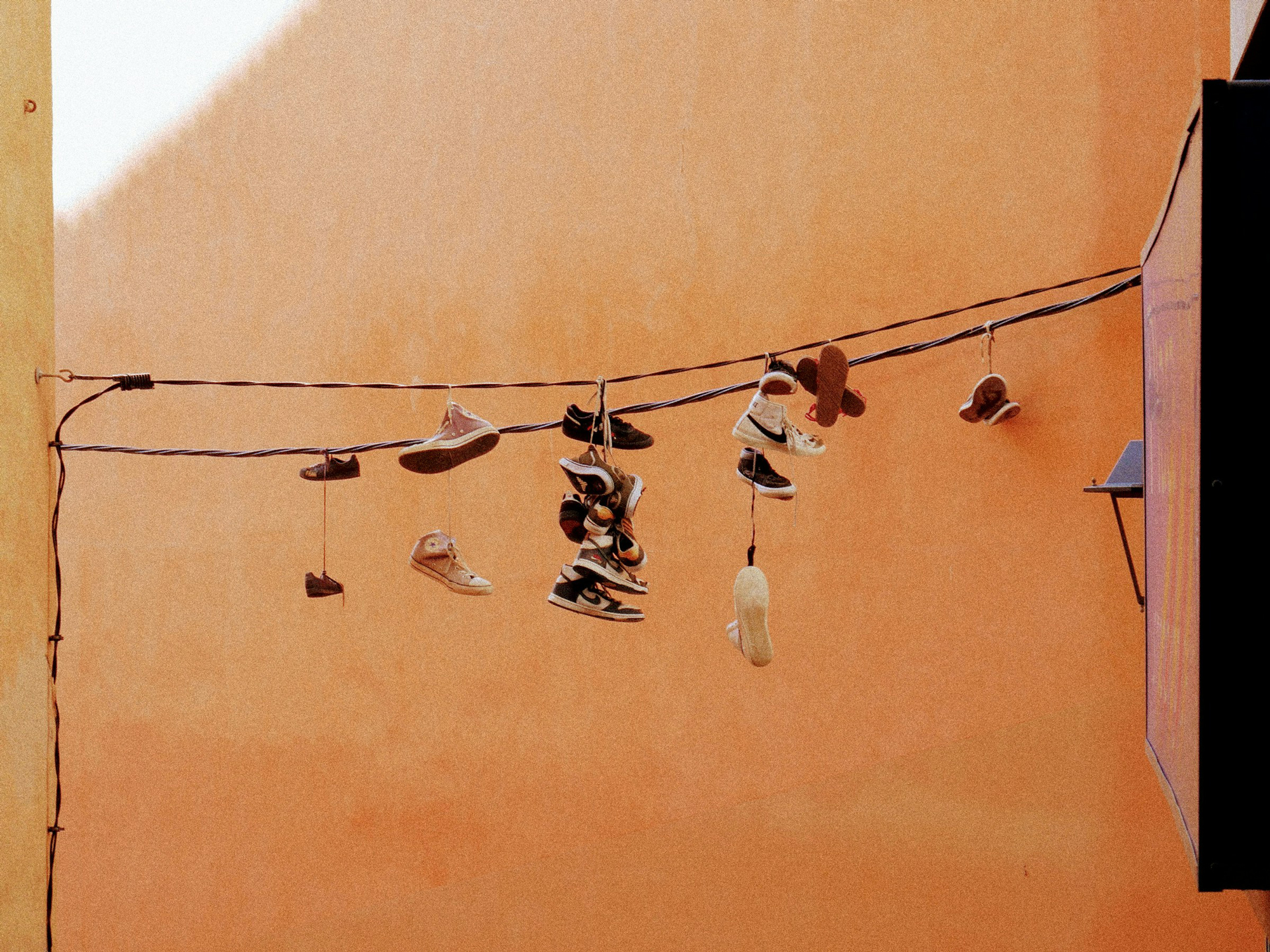 A collection of various shoes hanging from a wire against an orange wall background.