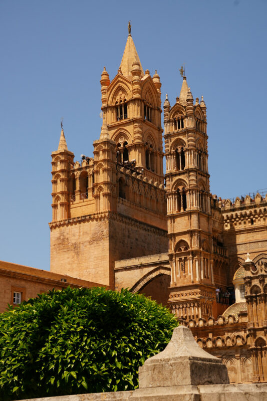 Historic cathedral towers in Palermo, featuring intricate architectural details against a clear blue sky.