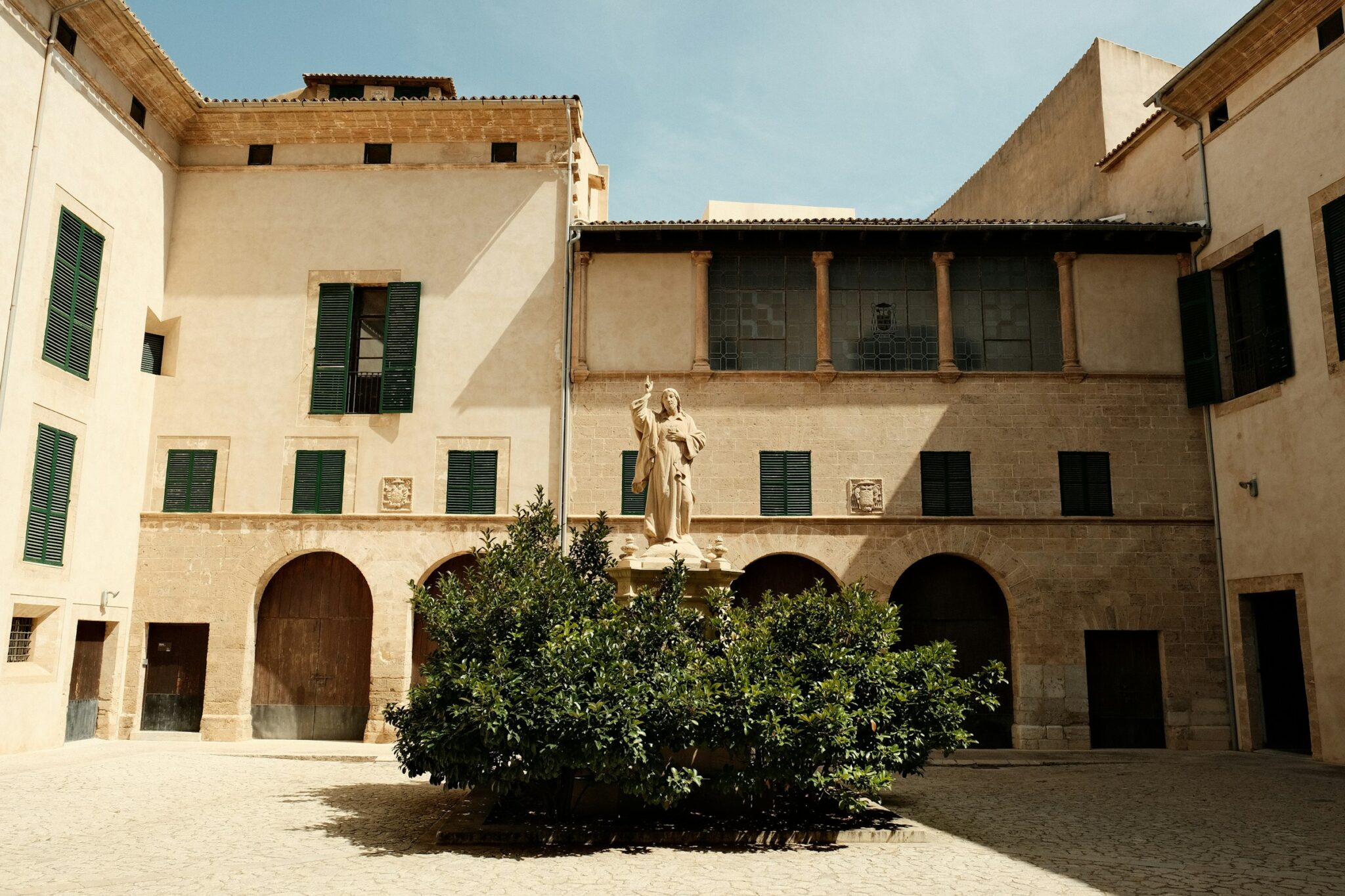 Stone statue in a courtyard surrounded by greenery and buildings with green shutters in Palma.