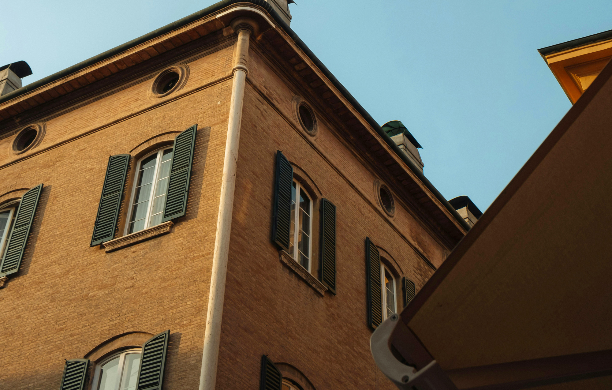 Brick building with green shutters and windows, viewed from below against a clear blue sky.