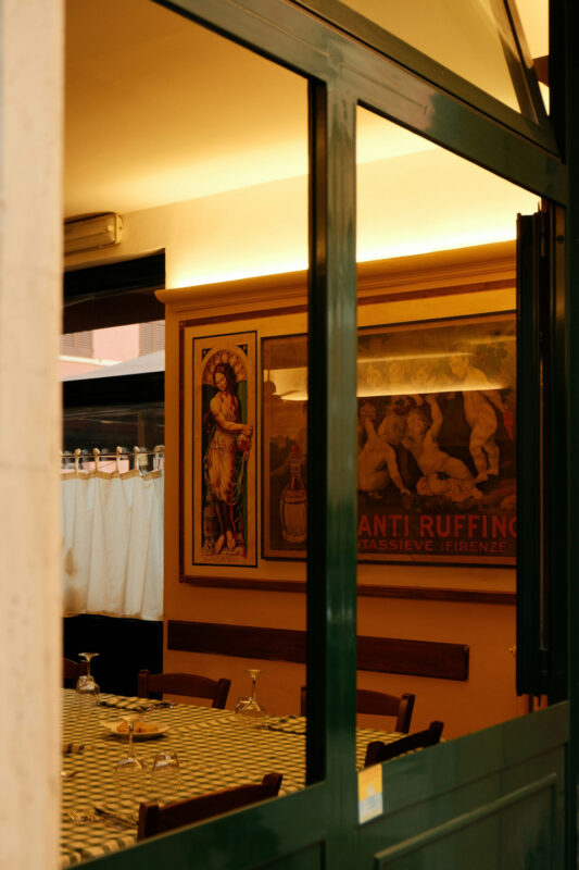 Interior of a restaurant featuring a green window frame, a checkered tablecloth, and vintage artwork on the walls.
