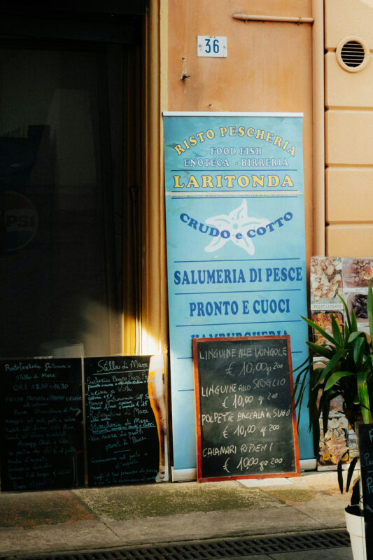 Colorful restaurant exterior featuring a seafood menu board and a large sign for "Risto Pescheria Lari tonda.