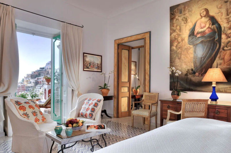 Elegant one-bedroom suite at Le Sirenuse, featuring sea view, cozy seating area, and a large religious painting.