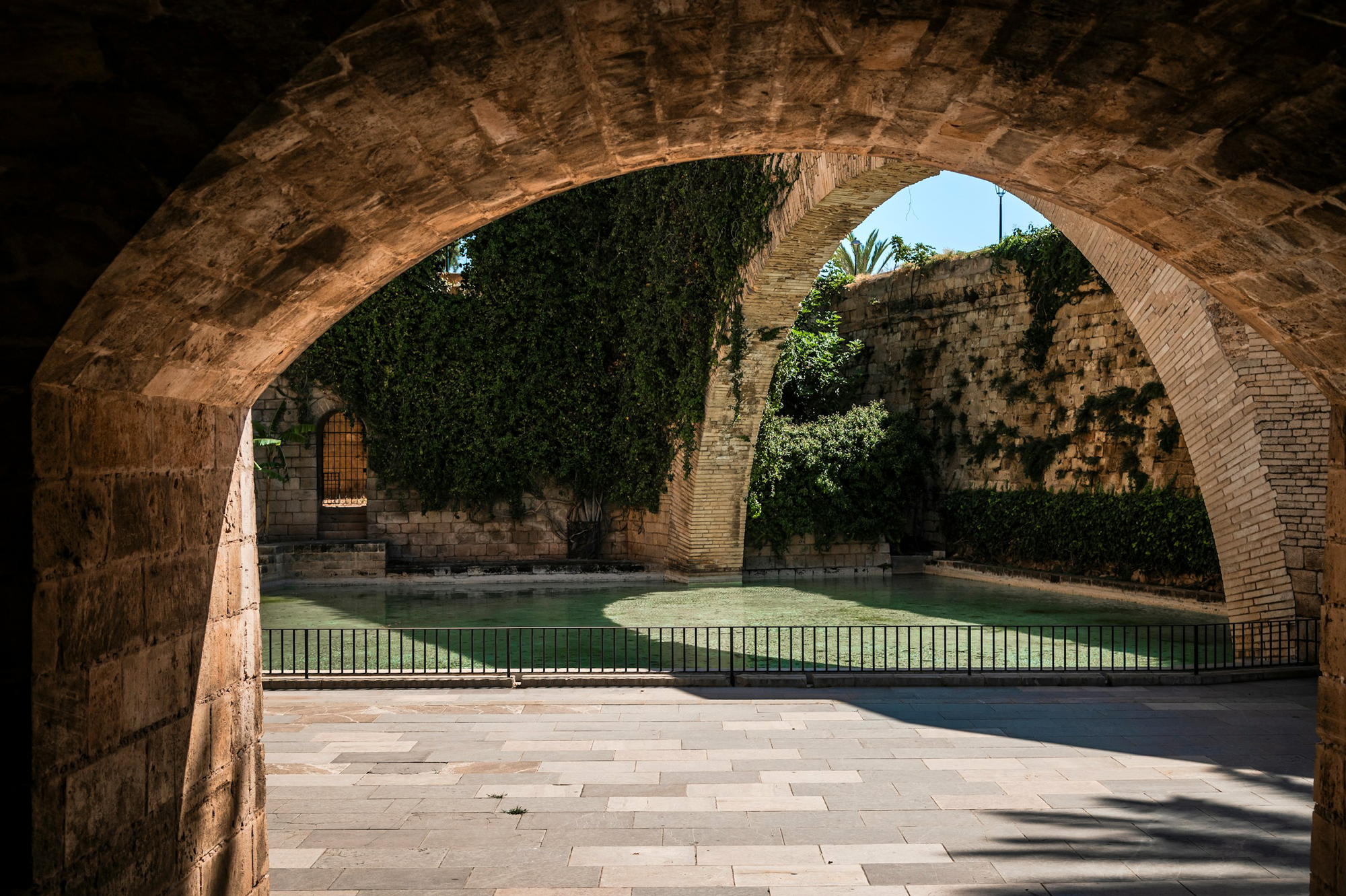 Stone archway framing a serene green pond surrounded by lush vegetation in Palma.