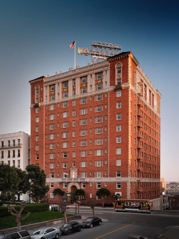 Historic Huntington Hotel exterior, a tall brick building with a flag atop, surrounded by trees and a street view.