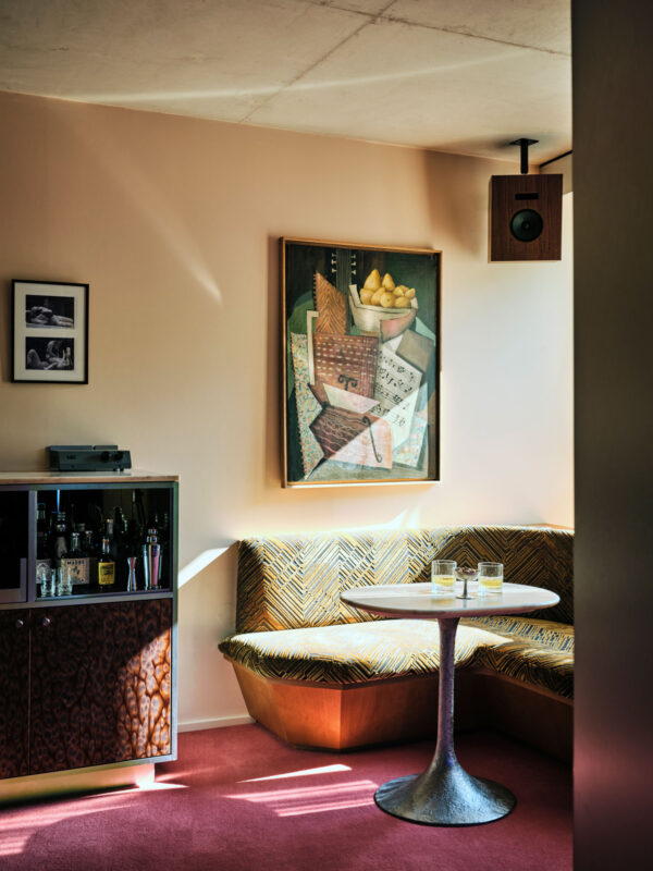 Cozy corner of a room featuring a curved brown seating area, a round table, and a colorful painting on the wall.