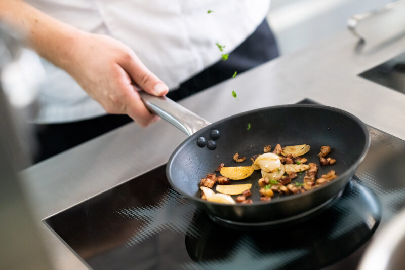 Sautéing vegetables and herbs in a black frying pan on a modern stovetop.
