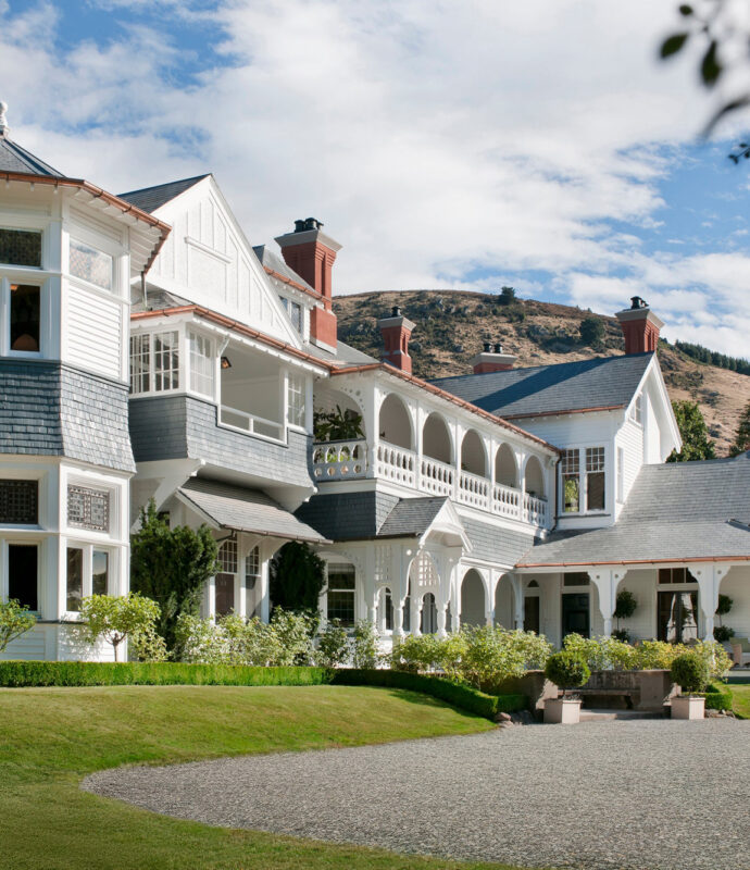 Elegant exterior of Otahuna Lodge featuring a mix of architectural styles, surrounded by manicured lawns and hills in the ...