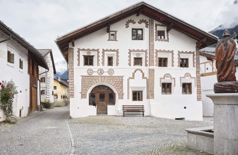 Historic white building with decorative brickwork, situated on a cobblestone street in a quaint village.