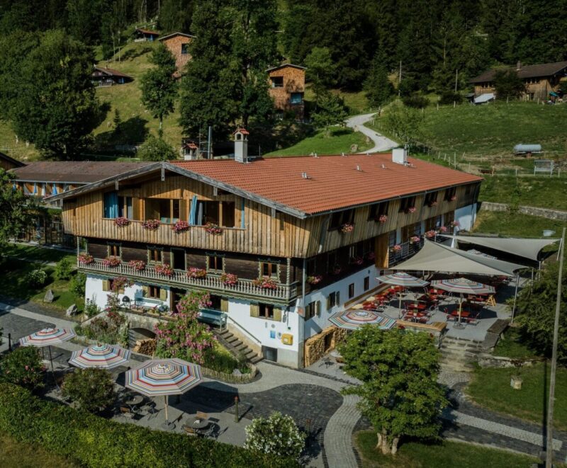 Scenic view of the Tannerhof building with a wooden facade, surrounded by greenery and colorful umbrellas on the terrace.